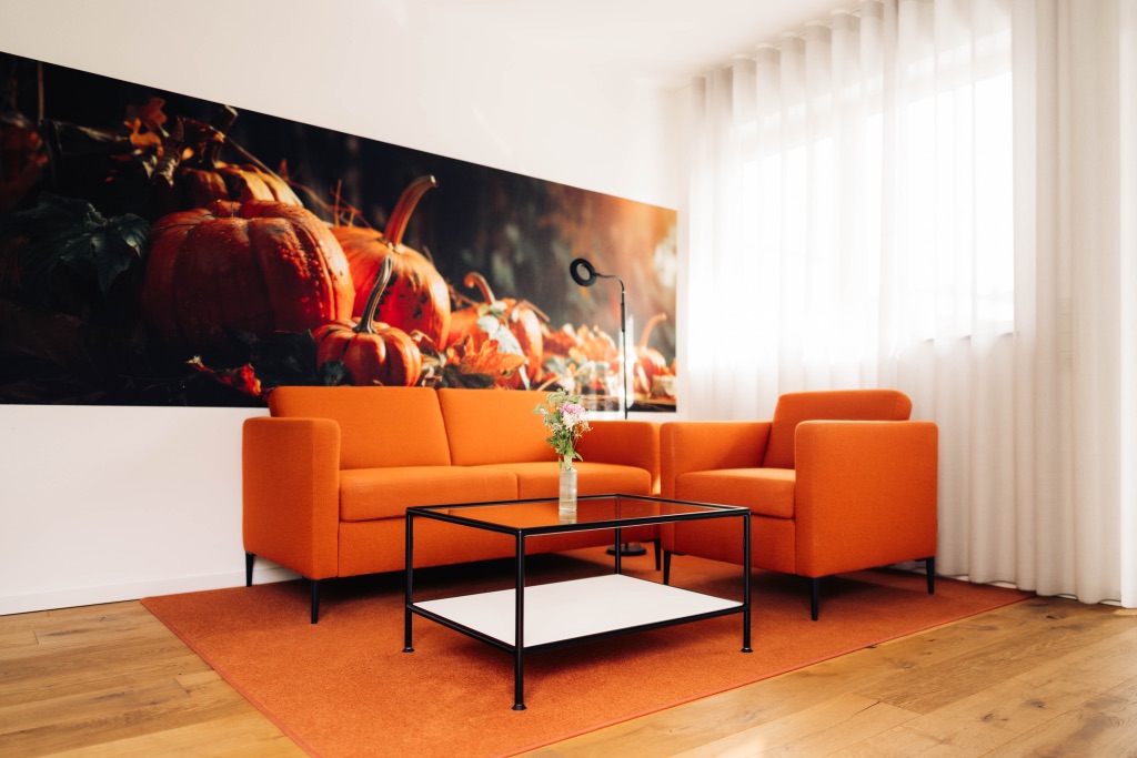 Wohnbereich mit orangefarbenem Sofa und Kürbis-Wandbild